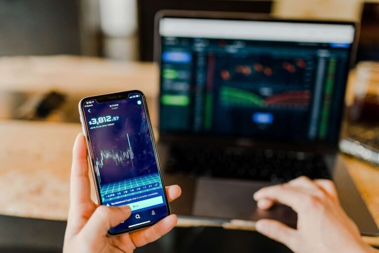 Person checking a stock trading app on a phone in front of a laptop