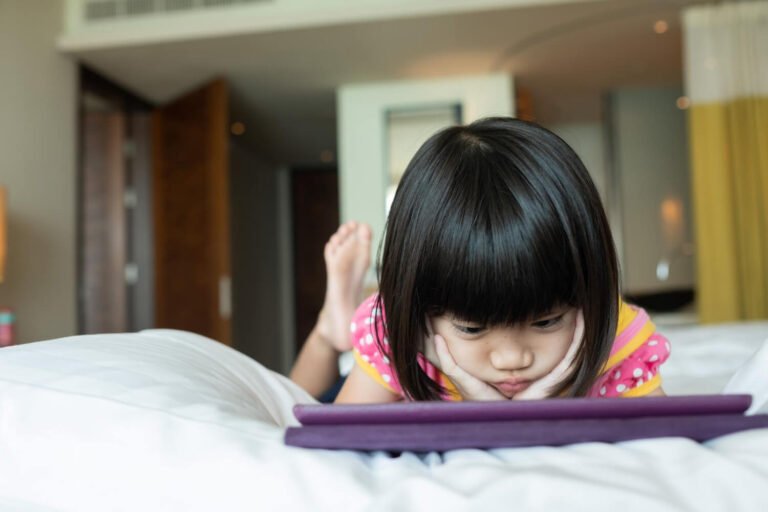 Child lying on a bed watching a tablet
