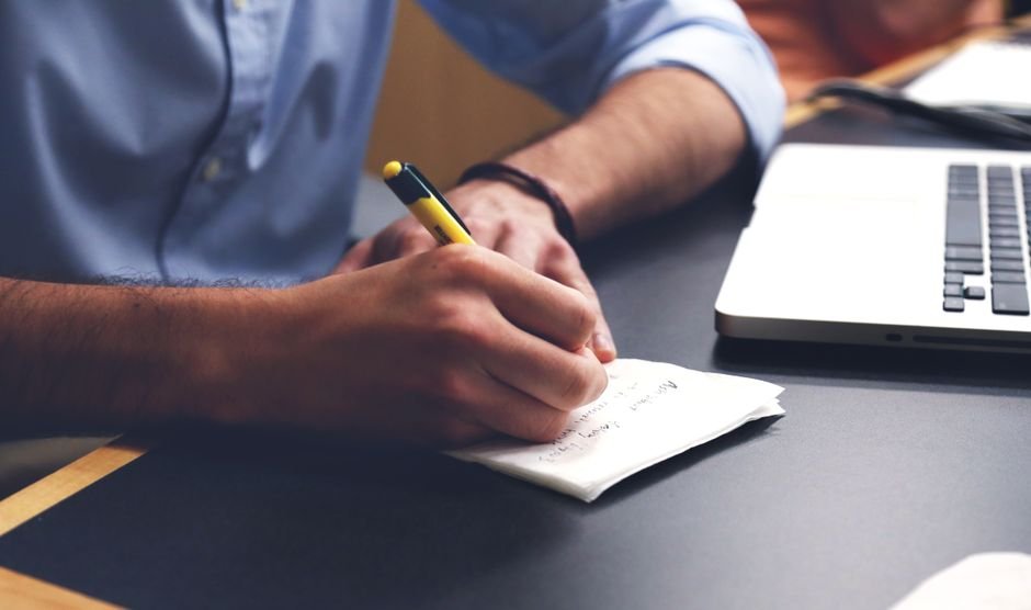 Freelancer logging AI experiment results in a notebook next to laptop