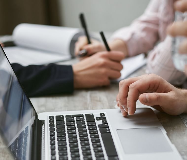 Person typing meeting agenda and notes on laptop during team discussion